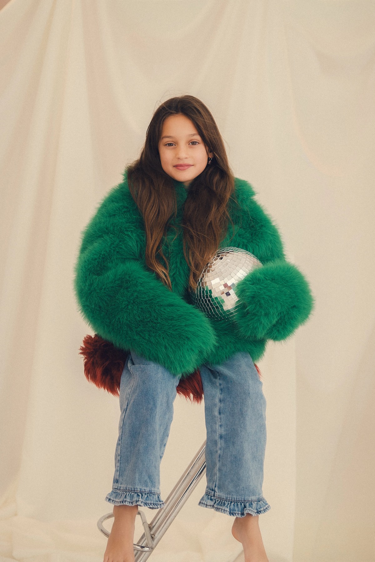 Meisje in een groene fluffy jas met een discobal