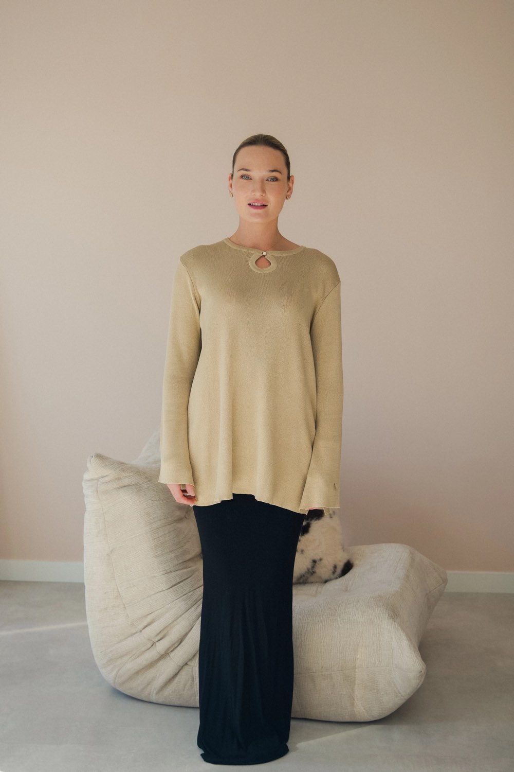 Vrouw in een beige gebreide jurk naast een togo-fauteuil in de studio