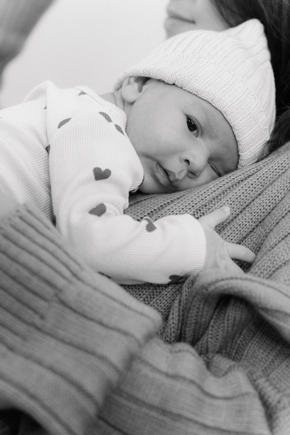 Newborn met mutsje op de borst van zijn ouder, zwart-wit