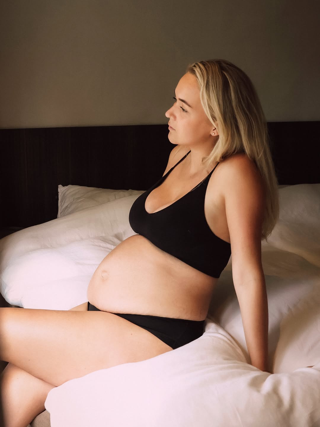Zwangere vrouw in zwarte lingerie op een wit bed
